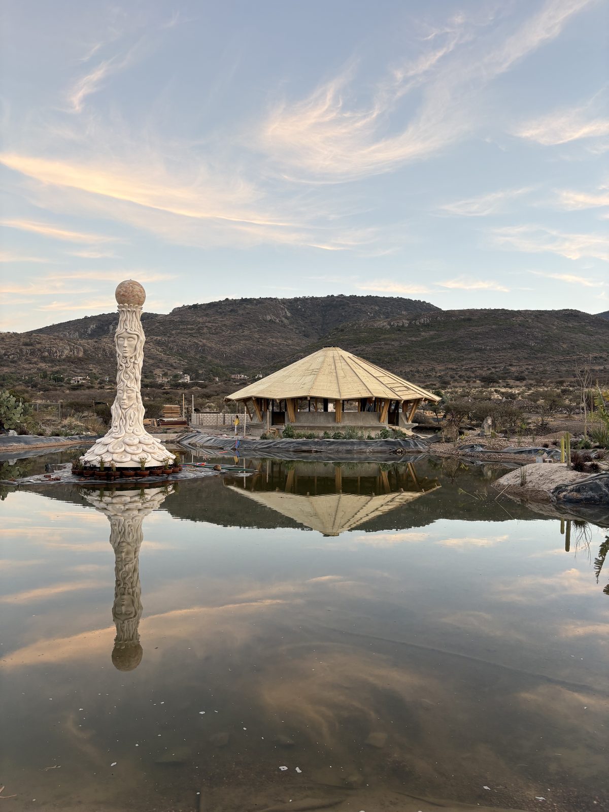 Shala ceremonial al atardecer con lago y escultura en Casa X